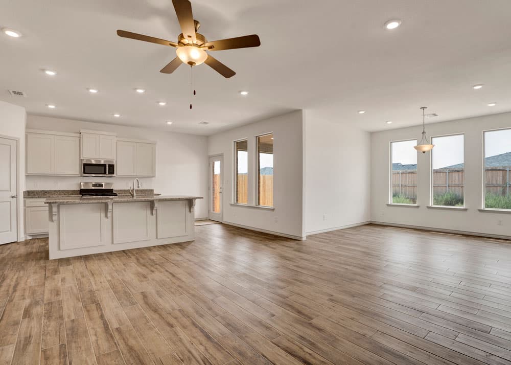 Open-concept living and kitchen area in a Shenandoah Ridge home featuring light wood floors, a ceiling fan, white cabinetry, a center island, stainless steel appliances, French doors, and large windows with outdoor views.